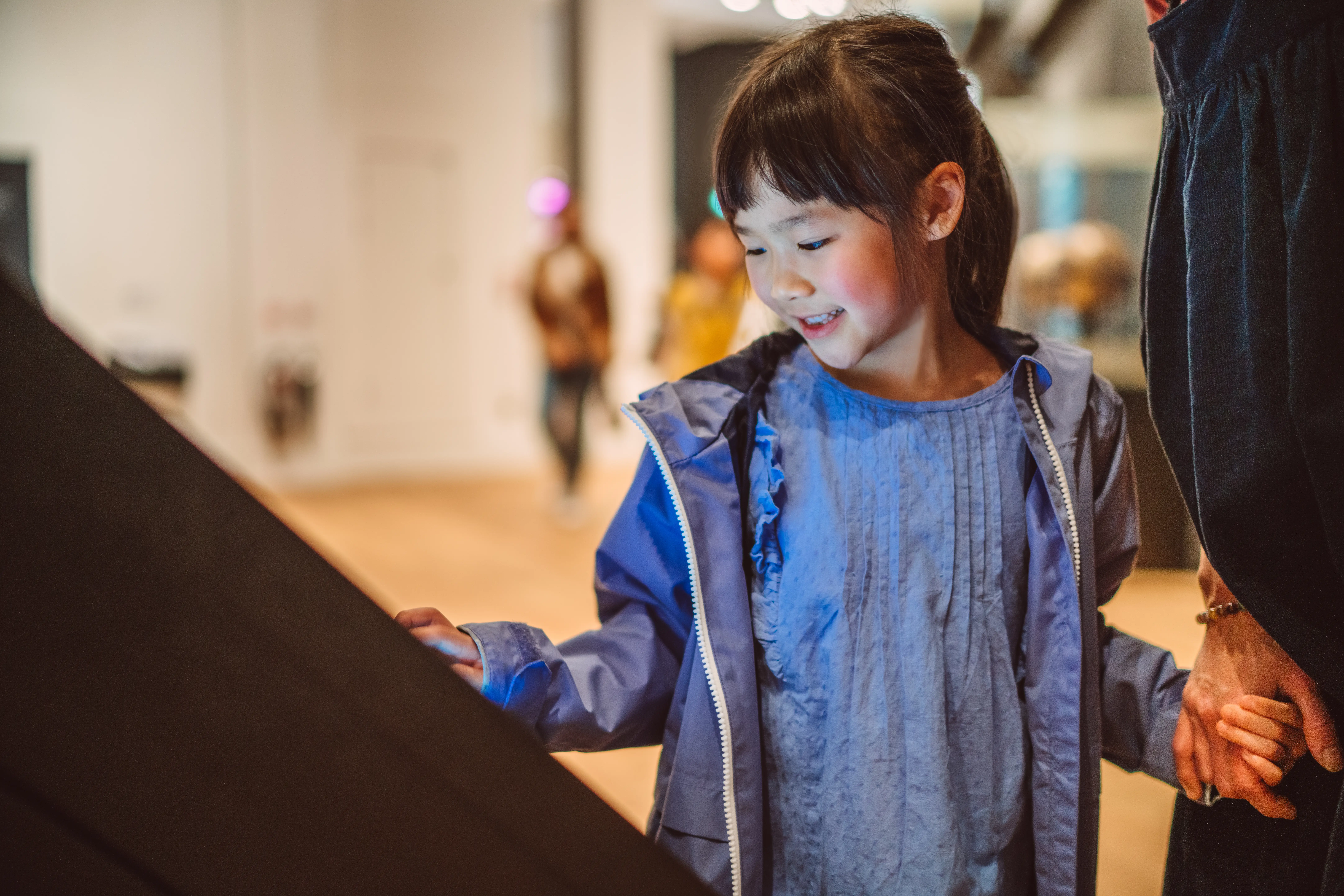 Lovely cheerful girl checking out exhibits with interactive touch screen in art gallery